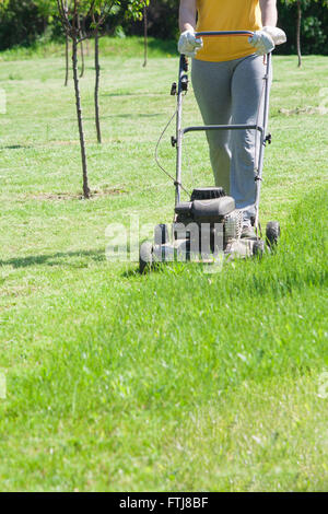 Junge Frau im Garten Rasen trimmen Rasenmäher schieben Stockfoto