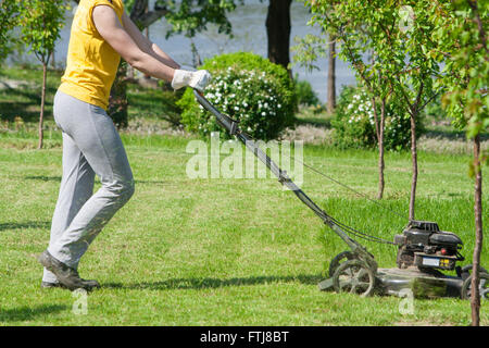 Junge Frau im Garten Rasen trimmen Rasenmäher schieben Stockfoto