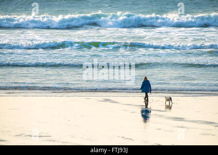Eine Frau, die ihren Hund am Fistral Beach in Newquay, Cornwall entlang der Küste läuft. Stockfoto