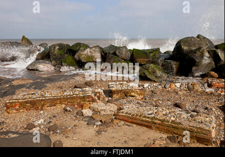 Wellen, die über Küstenschutzes mit gefallenen Gartenmauer im Vordergrund bei Happisburgh in Norfolk England UK Stockfoto