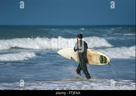 Eine Surfer trägt seinem Surfbrett geht er in das Meer am Fistral Beach in Newquay, Cornwall. Stockfoto
