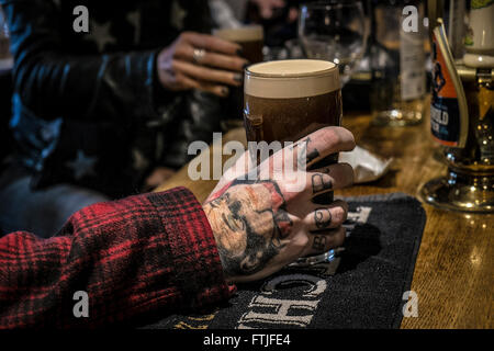 Kunden tätowierten Hand mit einem Pint Guinness in einem traditionellen englischen Pub in Essex. Stockfoto