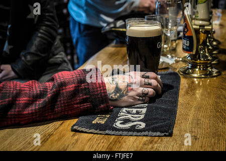 Kunden tätowierten Hand mit einem Pint Guinness in einem traditionellen englischen Pub in Essex. Stockfoto