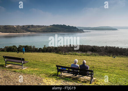 Ein paar sitzen auf einer Bank mit Blick auf den Fluss Camel in Padstow, Cornwall. Stockfoto