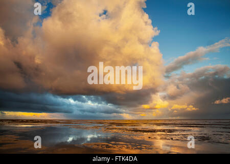 Southport, Merseyside, UK. Am 30. März 2016. UK Wetter. Gewitterwolken bilden über Meer, wobei ein dramatischer Sonnenaufgang über der Irischen See im nassen Sand und Strand pools refelcted. Stockfoto