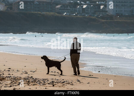 Ein Mann geht seinen Hund auf Fistral Beach in Newquay, Cornwall. Stockfoto