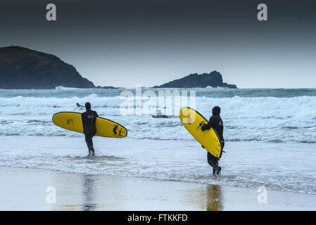 Zwei Surfer tragen ihre surfbretter auf dem Meer an einem kalten, kalten Tag an Fistral Beach in Newquay, Cornwall. Stockfoto