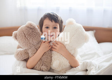 Süsser Boy mit Teddybären, im Bett liegend, Blick in die Kamera, Lächeln Stockfoto