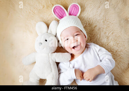 ein Jahr altes Baby liegend in Hase Hut auf Lamm Wolle Stockfoto