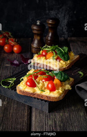 Toast zum Frühstück mit Rührei, Käse, Cherry-Tomaten, Rucola und Feldsalat auf rustikalen hölzernen Hintergrund Stockfoto
