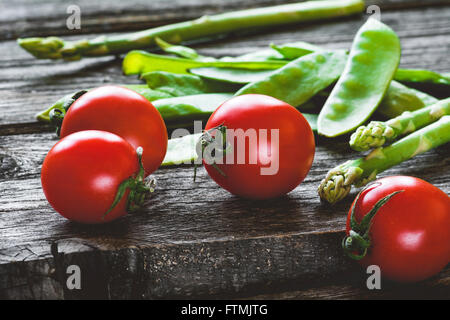 Cherry-Tomaten, Spargel und grünen Erbsenschoten auf rustikalen Holztisch, Nahaufnahme von frischem Gemüse Stockfoto