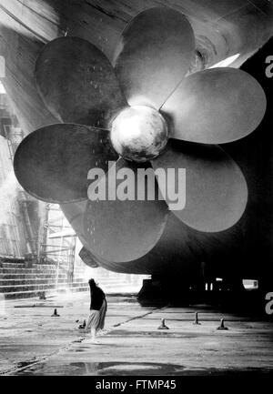 AJAXNETPHOTO. 1982. SOUTHAMPTON, ENGLAND. -FLOWER-POWER - RIESIGEN HAFEN PROPELLER VON CUNARD LINER QE2 DOMINIERT EINEN BESUCHER AUF DER KING GEORGE V DRY DOCK WO DER LINER VON FALKLAND TRUPPENTRANSPORTER PASSAGIER PFLICHTEN RESTAURIERT WURDE.   FOTO: JONATHAN EASTLAND/AJAX.  REF: HDD/SHI/LIN/QE2/PROP Stockfoto