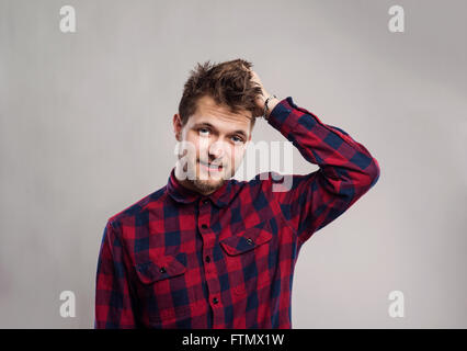 Hipster-Mann in überprüft Hemd lächelnd vor grauem Hintergrund. Stockfoto
