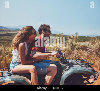 Seitenansicht der junge Mann und die Frau reitet auf einem Quad-Bike auf einen Sommerurlaub. Paar genießt Ferien auf einem Quad-Bike in countrysi Stockfoto