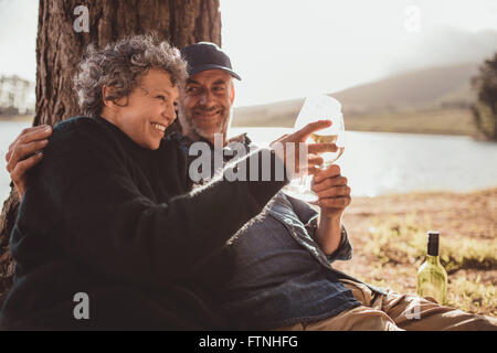 Porträt von senior Brautpaar sitzt in der Nähe von einem See Toasten mit Wein auf camping. Frau und Mann trinken Wein am Campingplatz. Stockfoto