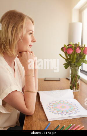 Seitenansicht des durchdachten Reife Frau sitzt an einem Tisch mit Erwachsenen Buch und Bleistifte Farben färben. Stockfoto