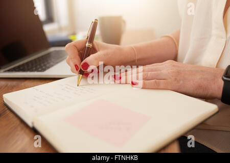 Schließen Sie herauf Bild der Frau Schreiben von Notizen in ihrem Tagebuch. Geschäftsfrau sitzt an ihrem Schreibtisch und wichtige Notizen in ihrer persönlichen Stockfoto