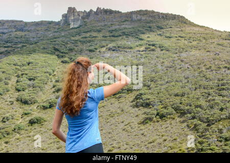 Mädchen auf einem Berg und sieht in der Entfernung mit einer Hand die Sonne zu blockieren Stockfoto