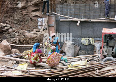 Drei indische Frau in hellen Sari und ein Kind ducken auf einem Haufen von Schutt und Bewehrung in einem indischen Baustelle Stockfoto