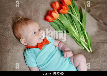 Kleiner Junge mit einem Strauß Tulpen auf dem Bett liegend Stockfoto