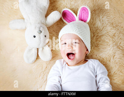 ein Jahr altes Baby liegend in Hase Hut auf Lamm Wolle Stockfoto