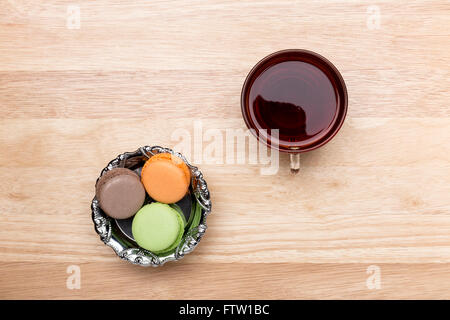 Glastasse schwarzer Tee und bunten Macarons auf hölzernen Hintergrund Stockfoto