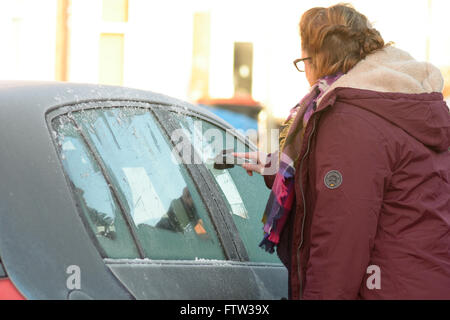 Frau Eis abschaben Autoscheiben an englischen frostigen Wintertag Stockfoto