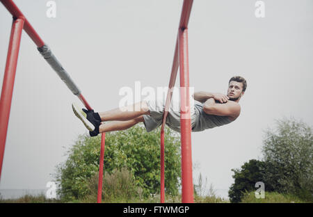 junger Mann tun Sit up auf Barren im freien Stockfoto