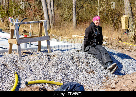 Ronneby, Schweden - 26. März 2016: Weibliche Bau Arbeiter sitzen auf einem Haufen Schotter in der Frühlingssonne ruhen. Haus gefunden Stockfoto