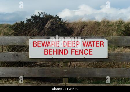 Schild mit der Aufschrift Vorsicht Tiefenwasser hinter Zaun Stockfoto