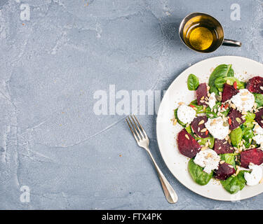 Salat mit gerösteten rote Beete, Spinat, weiche Ziege Heese und Samen in leichte Platte über grauen Beton strukturierten Hintergrund. Ansicht von oben Stockfoto
