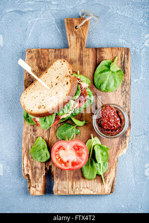 Huhn, getrockneten Tomaten und Spinat Sandwich mit pikanter Sauce auf rustikalem Holzbrett über grauem Beton strukturiertem Hintergrund, t Stockfoto