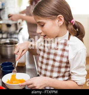 Kleinen Mädchens in Schürze schlagen von Eiern in weiße Schüssel in der Küche Stockfoto