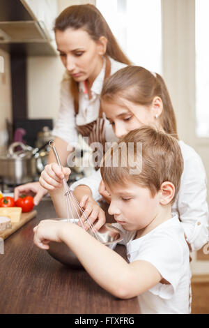 Familie kochen Hintergrund. Mutter und Kinder in der Küche. Kleiner Junge schlagen von Eiern in der Rührschüssel Stockfoto