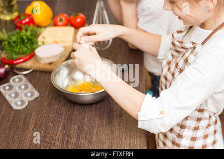 Kleinen Mädchens in Schürze Mischen von Eiern in weiße Schüssel in der Küche Stockfoto