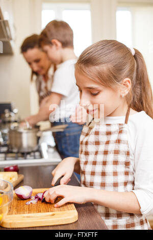 Familie kochen Hintergrund. Junge Teenager-Mädchen schneiden Zwiebel lächelnd. Mutter und Kinder in der Küche Stockfoto