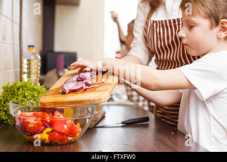 Familie kochen Hintergrund. Kleiner Junge mit schneiden Zwiebel Salat in der Küche seiner Mutter helfen Stockfoto