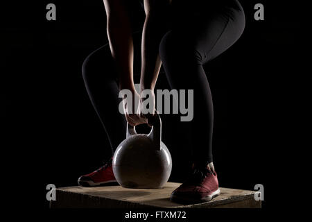 Junge Frau auf Holzkiste Kettlebell Krafttraining im Fitness-Studio Stockfoto