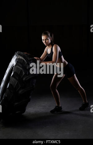 Junge Frau treibt einen LKW-Reifen in der Turnhalle Stockfoto