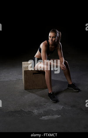 Junge Frau sitzt auf Holzkiste im Fitness-Studio Stockfoto