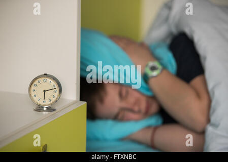 Junge im Bett für seine Ohren beim Wecker klingeln Stockfoto