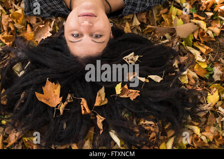 Frau auf dem Boden liegend mit Herbst Blätter in ihr langes Haar Stockfoto