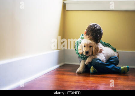 Junge sitzt auf Boden, umarmt golden Retriever Welpe Hund Stockfoto