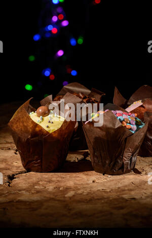 Vier Schokoladen-Muffins mit Glasur und bunten Süßigkeiten dekoriert Stockfoto