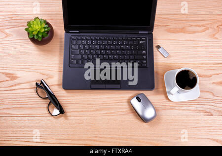 Draufsicht auf einen sauberen Schreibtisch bestehend aus Laptop, Babypflanze, Maus, USB-Stick, Kaffee und Lesebrille. Stockfoto