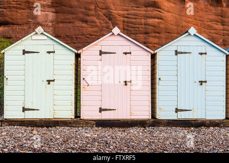 Strandreihe Hütte in Pastell-Farben, rote Felsen Hintergrund, South Devon, UK Stockfoto