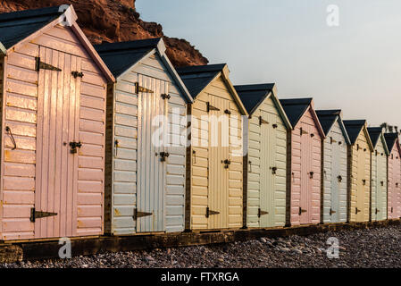 Strandreihe Hütte in Pastell-Farben, rote Felsen Hintergrund, South Devon, UK Stockfoto