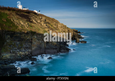 Trinity Leuchtturm an der Felsenküste in Cornwall, Großbritannien. Wiev bei Sonnenuntergang mit Bewegung Wellen, Luftbild. Stockfoto