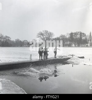 1950er Jahre historische, erfrischen Winterzeit und tapferen Gefährten im Schnee bedeckte Männer nur Süßwasser Teich in Hampstead Heath, London. Stockfoto