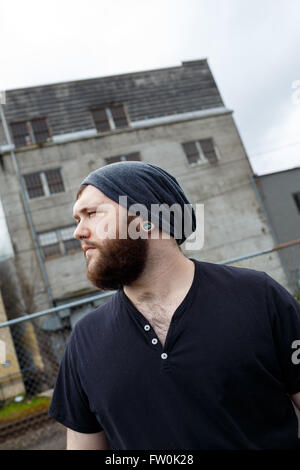 Junger Erwachsener Mann im Freien in einem städtischen Umfeld für Lifestyle Portrait eines bärtigen Hipster. Stockfoto